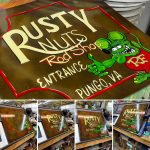 “Hand‑painted Rat Fink–inspired shop sign with bold cartoon lines, bright colors, and traditional hot rod style.”